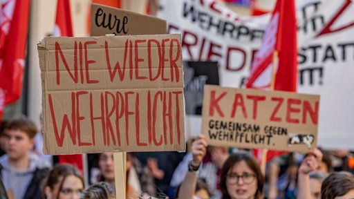 Junge Menschen laufen nebeneinander und halten Schilder hoch, auf einem steht in roter Schrift "Nie wieder Wehrpflicht"