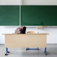 Schultafel in einer Klasse und davor steht ein Pult auf dem eine Tasche steht