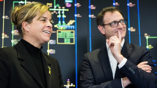 Zwei lachende Personen vor einer digitalen Wand mit Leitungen