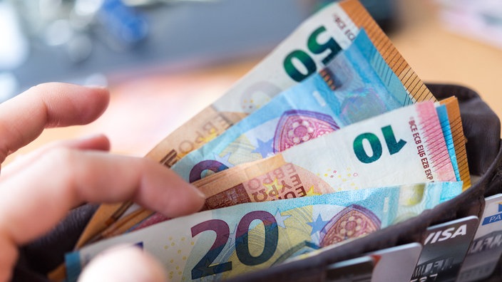  Eine Hand hält eine Geldbörse mit zahlreichen Banknoten und Bankkarten in der Hand.