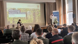 Silke Gorißen, Ministerin für Landwirtschaft und Verbraucherschutz, stellt bei einer Pressekonferenz auf einer Bühne an einem Rednerpult die Waldstrategie NRW vor.
