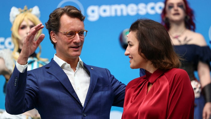Wüst und Baer unterhalten sich auf der Gamescom, im Hintergrund sind Cosplayer zu sehen