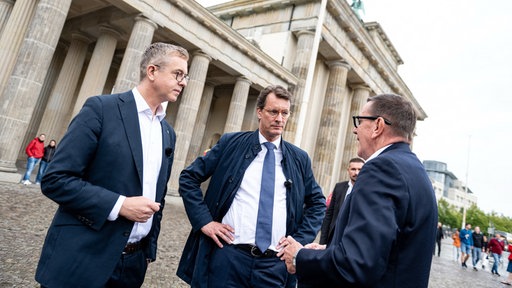 Stefan Evers, Hendrik Wüst und Mario Röllig im Gespräch miteinander vor dem Brandenburger Tor.