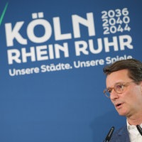 Hendrik Wüst vor dem Logo der Olympischen Spiele an Rhein und Ruhr