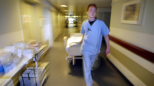 Ein junger Mann zieht ein Krankenbett durch einen Krankenhausflur.