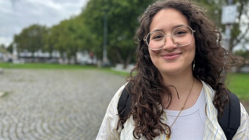 Eine junge Frau mit Brille lächelt in die Kamera.