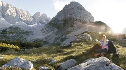 Mutter liest ihrer Tochter auf einer Bergwiese etwas vor