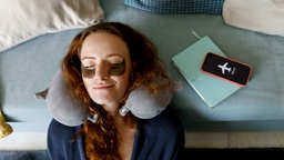 Rothaarige Frau lehnt Kopf an Sofa, Smartphone im Flugmodus.