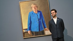 Das Portraet der frueheren Bundeskanzlerin Angela Merkel. Gemalt wurde es von dem deutsch-franzoesischen Maler Jeremie Queyras (Foto), der Merkel stehend und in einem blauen Blazer portraetiert hat.