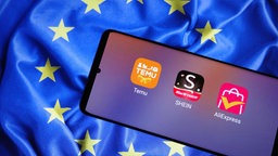 Symbolbild: Ein Smartphone mit den Apps von Temu, Shein und Ali-Express vor einer EU-Fahne.