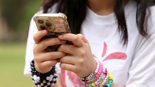 Eine junge Australierin mit bunten Armbändern hält ein Smartphone in den Händen.