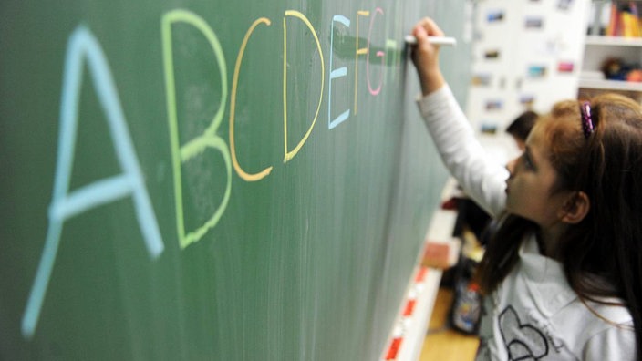 Ein Mädchen schreibt das ABC auf eine Schultafel