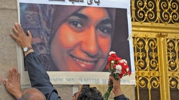 ARCHIV - Vor dem Rathaus in Dresden (Sachsen) kleben zwei Männer ein Foto der am 01.07.2009 im Dresdner Landgericht erstochenen Ägypterin Marwa El-Sherbini an die Wand 