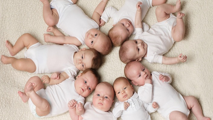 Babys, die auf einer Decke liegen und mit ihren Köpfen einen Kreis bilden.