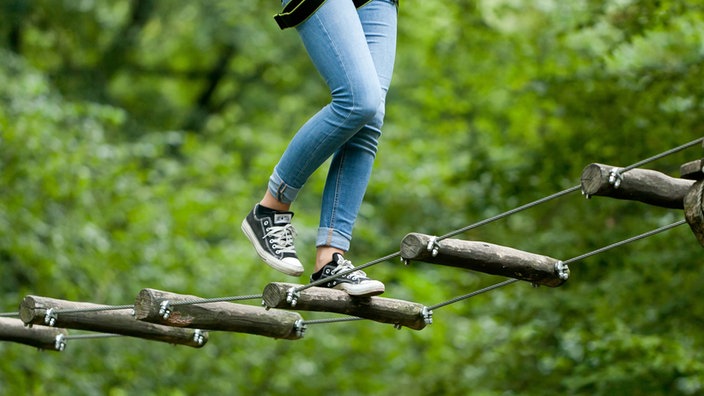 Beine einer jungen Frau beim aktiven Klettern im Hochseil-Garten.
