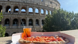 Eine Pizza und ein Aperol, im Hintergrund das Colosseum