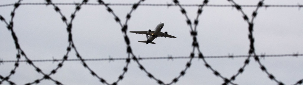 Ein Flugzeug im Himmel durch einen Stacheldraht gesehen