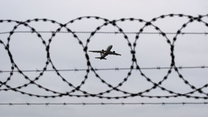 Ein Flugzeug im Himmel durch einen Stacheldraht gesehen