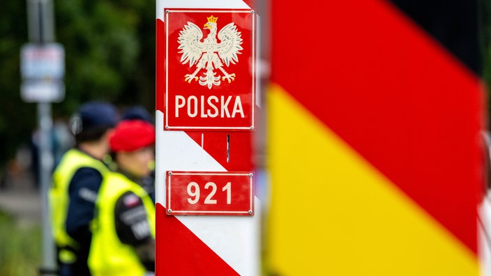 Polski słup graniczny na tle pograniczników i niemieckiej flagi