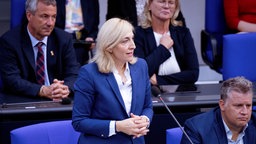 Bundesgesundheitsministerin Nina Warken (CDU) steht an ihrem Platz auf der Regierungsbank und spricht ins Mikrofon (Nahaufnahme), drumherum sitzen weitere Personen