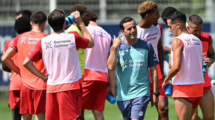 Leverkusens Trainer Carles Martínez Novell (mittig, mit zwei Fingern deutend) inmitten von Spielern beim Training im sonnigen Stadion