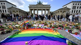 Am Brandenburger Tor in Berlin liegen rund um eine Regenbogenflagge Blumen und Kerzen nach dem tödlichen Anschlag beim CSD am 25.07.27 (Foto vom 27.07.2026)