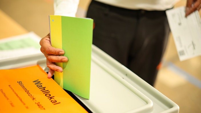 Ein Mann wirft am 14.09.2025 seine Stimmzettel in eine Wahlurne in einem Duisburger Wahllokal.
