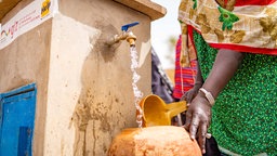 Eine Frau füllt ein Gefäß mit Wasser
