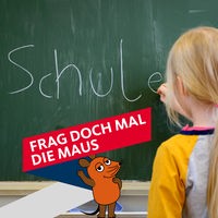 Ein Mädchen schreibt das Wort "Schule" an eine Tafel