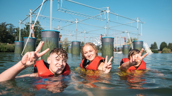 Aqua-Climb in Selm: Drei junge Leute mit Schwimmwesten sind lächelnd im Wasser