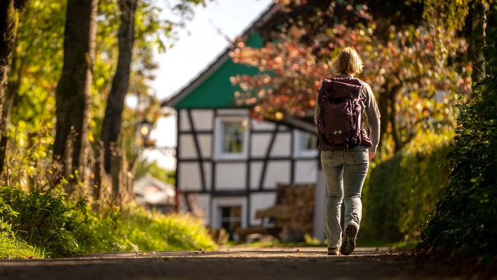 Eine Wanderin läugt über einen Weg auf ein Fachwerkhaus zu.
