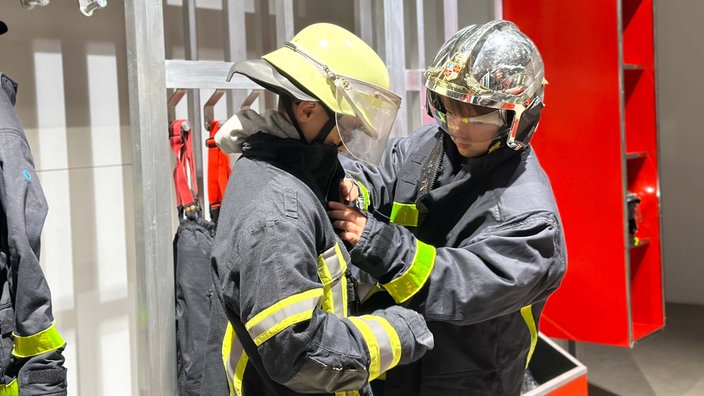 Zwei Ausstellungsbesucher probieren in der DASA-Ausstellung "Feuer" Feuerwehrkleidung an.