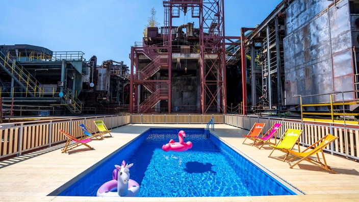 Im Becken des Werksschwimmbads auf Zollverein schwimmen aufblasbare Gummitiere, drumherum die alte Industriekulisse