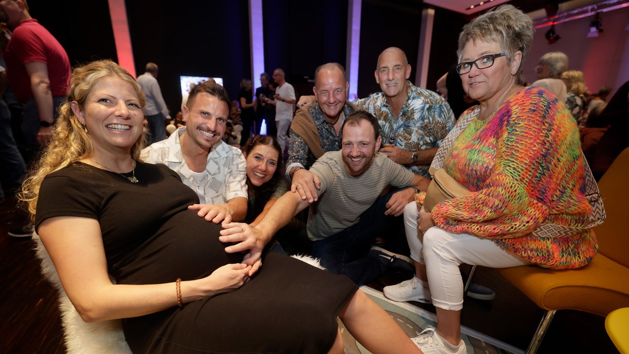 Mehrere Menschen halten den Babybauch einer schwangeren Frau bei der WDR 2 Hausparty in Siegburg