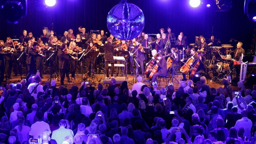 Blick auf die Bühne bei der WDR 2 Hausparty in Siegburg. Dort sitzt das Ensemble des WDR Funkhausorchesters. Von der Decke hängt eine Discokugel