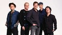 Die Toten Hosen stehen zusammen in einem leeren Raum und lächeln in die Kamera