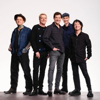 Die Toten Hosen stehen zusammen in einem leeren Raum und lächeln in die Kamera