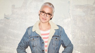 Die Sängerin Stefanie Heinzmann steht vor einer grauen Betonwand, hat die Hände in den Jackentaschen 