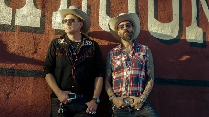 The BossHoss stehen mit Sonnenbrillen vor einer Wand.