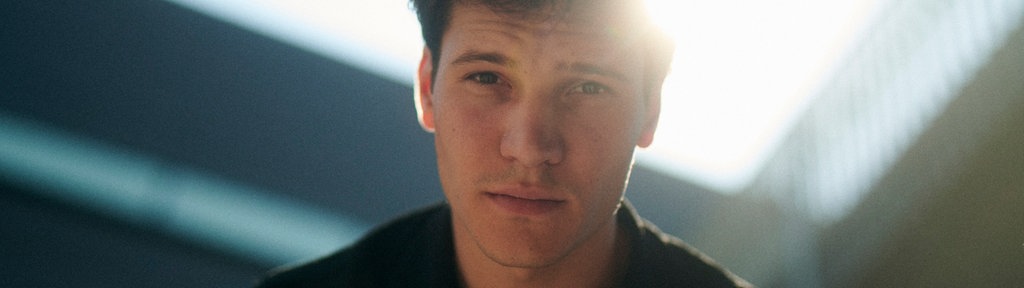Eine Nahaufnahme von Wincent Weiss lächelnd vor einer weißen Wand