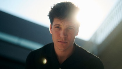 Eine Nahaufnahme von Wincent Weiss lächelnd vor einer weißen Wand