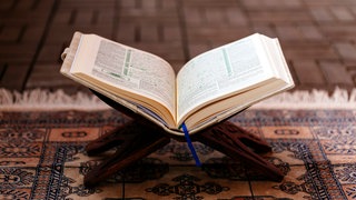 Symbolbild: Ein Koran in einer Halterung auf einem Gebetsteppich