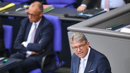 Weimar spricht am 24.09.2025 im Deutschen Bundestag bei der 27. Bundestagssitzung zur Haushaltswoche. Im Hintergrund sitzt Bundeskanzler Friedrich Merz mit verschränkten Armen.