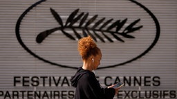 Eine Frau geht vor den 79. Internationalen Filmfestspielen in Cannes am Schild des Filmfestivals von Cannes vorbei.
