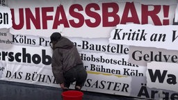 "Frustzaun" an der Oper Köln: Ein Bauzaun an dem auf Plakaten Worte wie "Unfassbar", "Bühnendesasater", "Kritik" prangen.