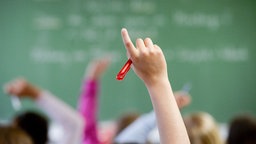 Ein Klassenzimmer - Schülerinnen und Schüler strecken die Finger zur Meldung in die Höhe