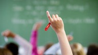 Ein Klassenzimmer - Schülerinnen und Schüler strecken die Finger zur Meldung in die Höhe