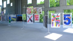 Ausstellungsansicht "100 Beste Plakate 2025" im Museum Folkwang in Essen: Mehrere unterschiedliche Plakate hängen an Ständern nebeneinander.