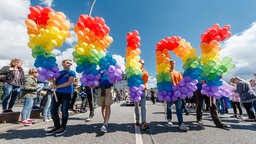 Symbolbild: Menschen auf einer Christopher-Street-Day Parade mit Luftballons in Regenbogenfarben, die das Wort "PRIDE" formen.
