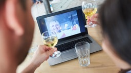 Symbolbild: Paar feiert virtuell Geburtstag im Videochat und stößt vor der Kamera mit Gläsern an.